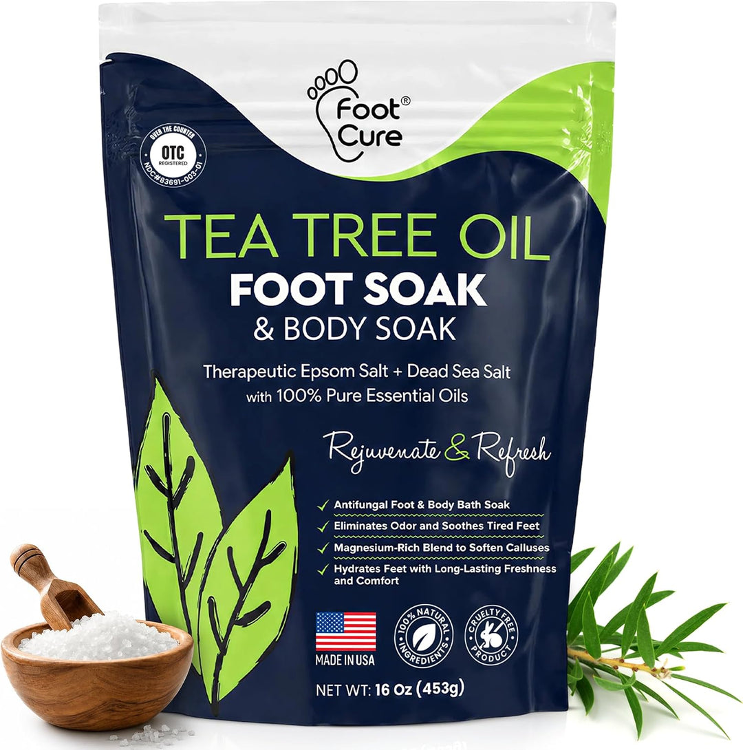 A stand-up pouch of Foot Cure Tea Tree Oil Foot Soak & Body Soak on a white background, with a small wooden bowl of salt and tea tree branches shown at the bottom corners.