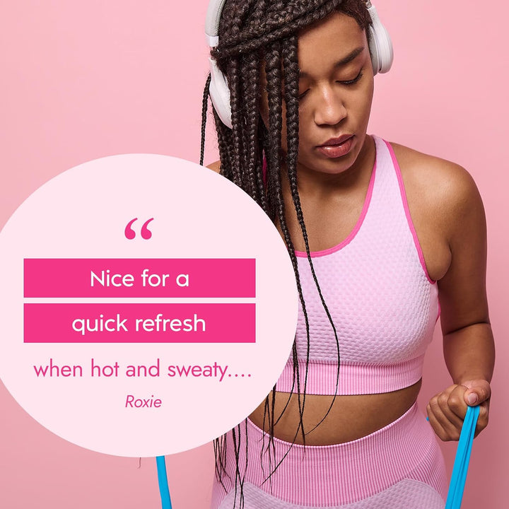 A woman in a pink sports bra and matching leggings with white headphones, holding blue resistance bands against a pink background, with a large quote bubble overlay reading 'Nice for a quick refresh when hot and sweaty.