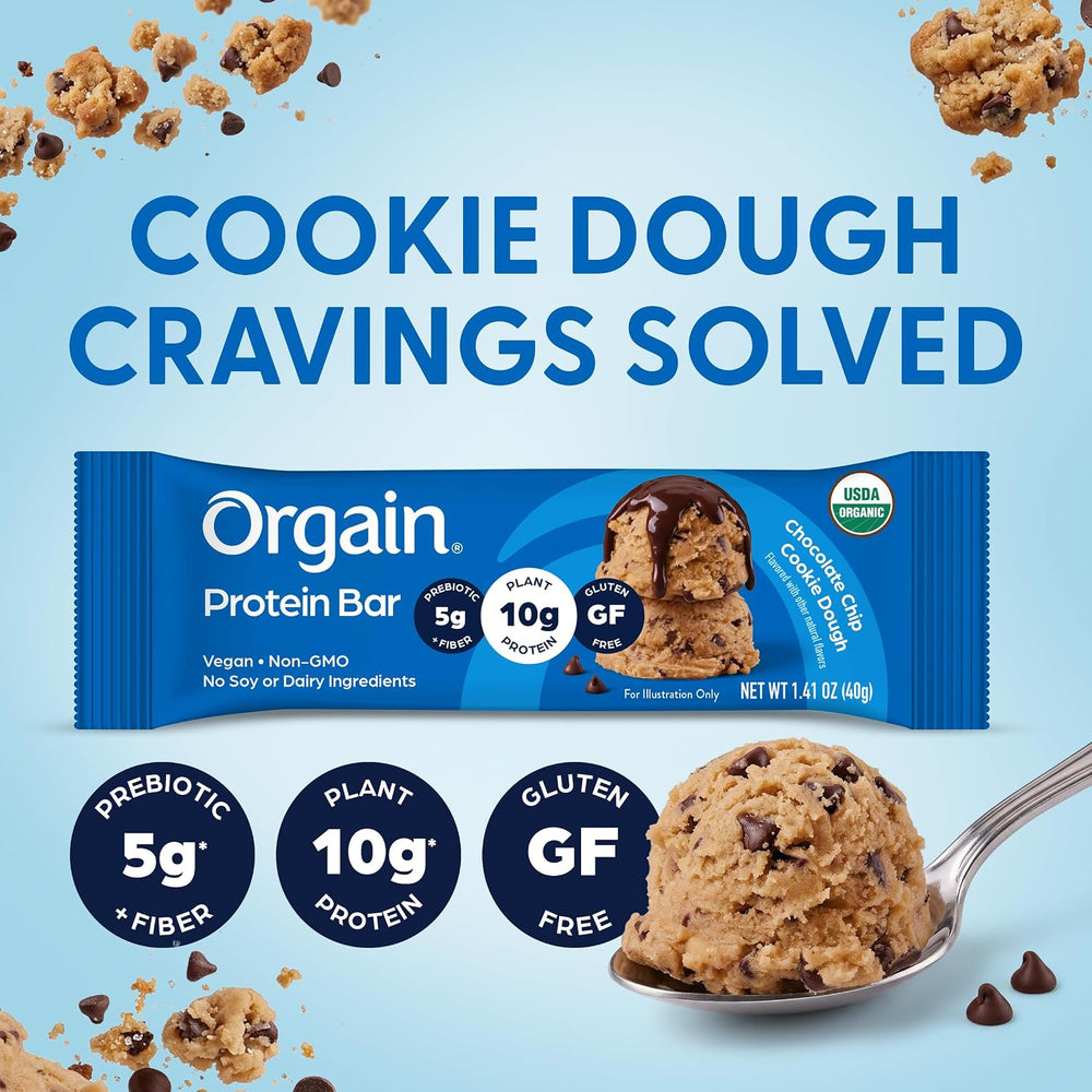 Orgain Cookie Dough Protein Bar package on a light blue background with cookie dough crumbs, a spoonful of cookie dough, and large text reading 'COOKIE DOUGH CRAVINGS SOLVED.'.