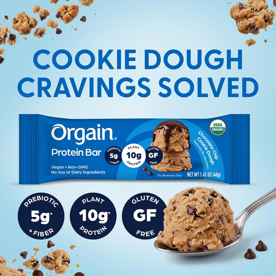Orgain Cookie Dough Protein Bar package on a light blue background with cookie dough crumbs, a spoonful of cookie dough, and large text reading 'COOKIE DOUGH CRAVINGS SOLVED.'.