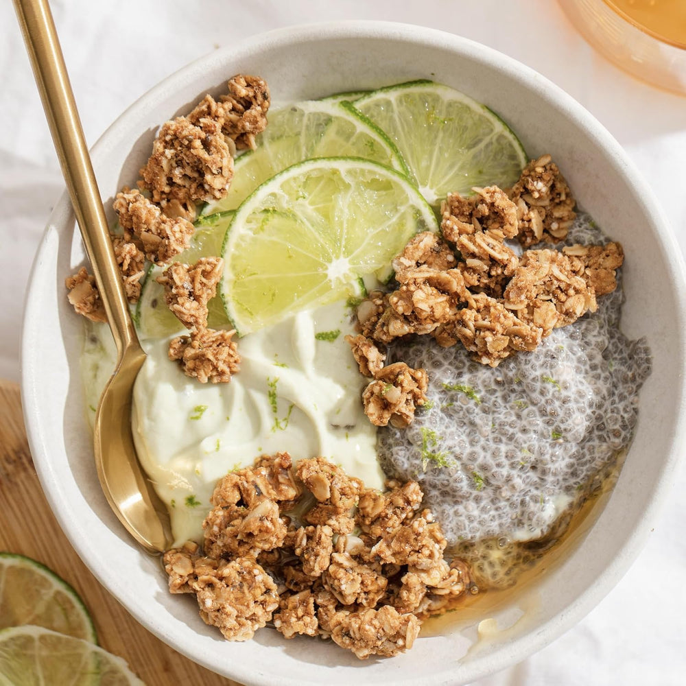 Yogurt bowl with granola, lime slices, and chia seeds in a white bowl with a gold spoon.